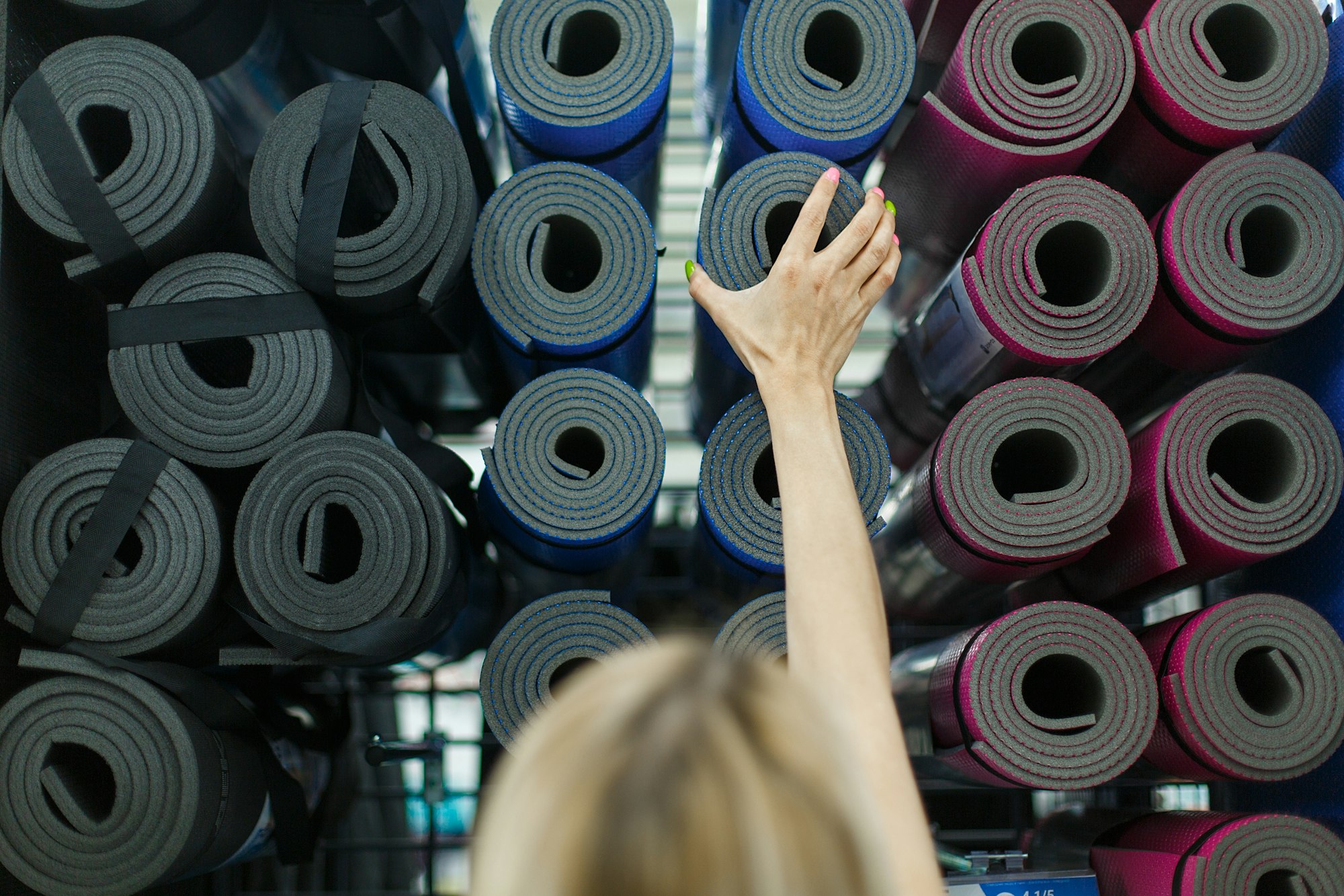 Young woman in sports store buys yoga and fitness mat. He takes out a sports mat from the shelf.