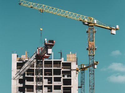 Construction Crane Is Involved In The Construction Of A New Multi-storey Residential Building. Sunny Summer Day. Construction Crane On Background Of Blue Sunny Sky.